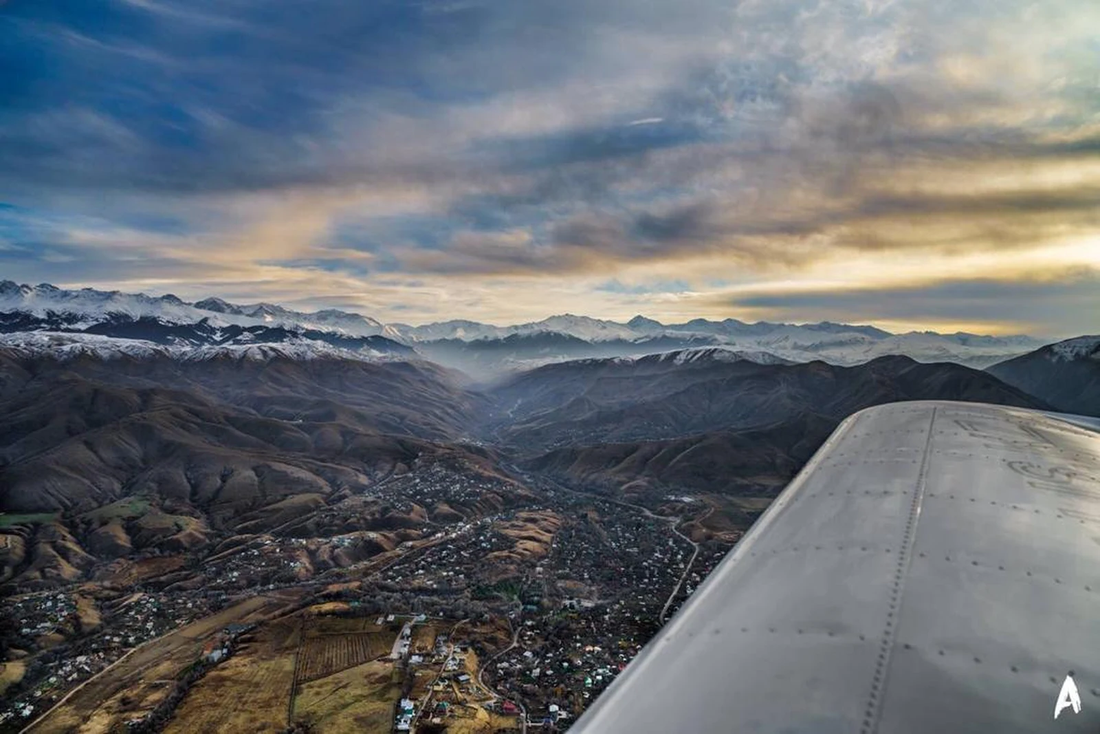 Aerial view of Almaty city and the snow-capped Tien Shan mountains from a plane wing at sunset